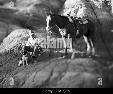 Coppia cowboy seduto su una roccia grande roccia accanto al suo cane e cavallo all'esterno. Foto Stock