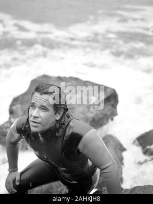 Uomo in wetsuit salendo su rocce dopo arrivare al di fuori dell'acqua. Foto Stock