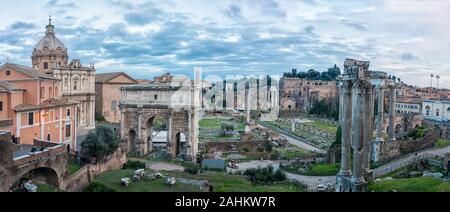 Vista panaromica al tramonto delle rovine del foro romano con l'Arco di Settimio Severo esposto in modo prominente. Foto Stock