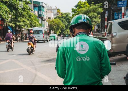 Un Grab Bike Rider controlla il loro telefono in attesa del processo successivo ad Hanoi, Vietnam. Grab è il Sud Est Asiatico più popolare ride salutando e app per la consegna Foto Stock