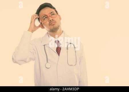 Studio shot del giovane uomo asiatico del pensiero medico mentre la testa di graffiatura Foto Stock