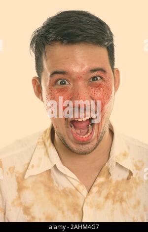 Volto del giovane pazzo uomo asiatico urlando con il sangue sulla faccia Foto Stock