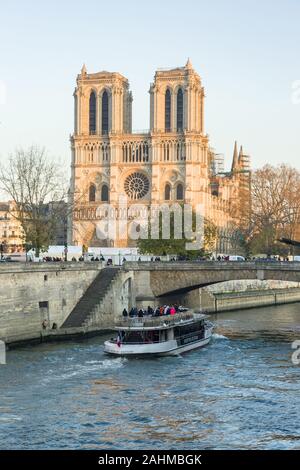 Esterno della Cathédrale Notre-dame de Paris con la nave da crociera sul fiume Senna in primo piano su una soleggiata giornata invernale, Parigi, Francia Foto Stock