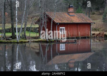 Piccolo rosso in legno antico lavatoio vicino al coperto di ghiaccio sul lago. Foto Stock