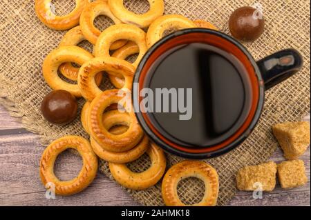 Piccole ciambelle, cioccolatini, una tazza di tè e una ruvida stoffa homespun su uno sfondo di legno di close-up Foto Stock