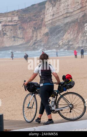 Turista femminile sulla gita in bicicletta con la sua bicicletta sulla spiaggia di nazare, Portogallo Foto Stock