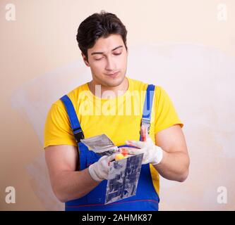 Il giovane dipendente del contraente di applicare gesso sulla parete Foto Stock