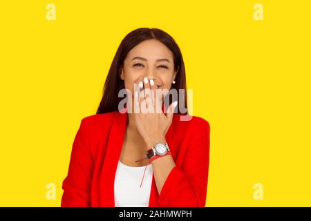 Bella donna ridendo e guardando a voi fotocamera, con la mano che copre la sua bocca. Razza mista modello isolato su sfondo giallo con copia spazio. Hori Foto Stock