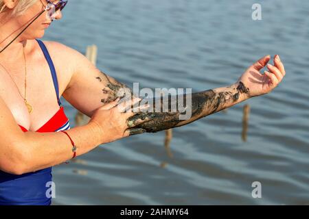 Donna applicando sul suo corpo salato fango curativo sul braccio nel lago Foto Stock