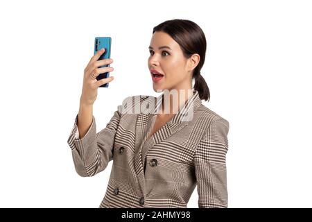 Giovane donna in grigio tuta a scacchi tenuto selfie, isolato su bianco, spaventato di fronte Foto Stock