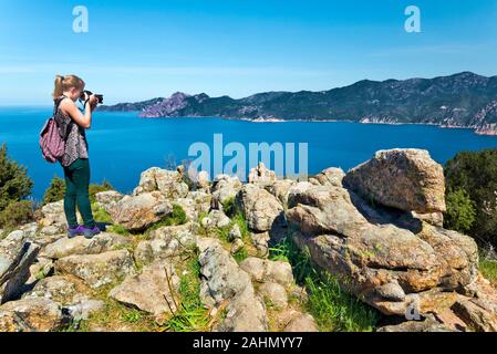 Ragazzina prende foto della baia di Porto in Corsica da Calanques de Piana, il paesaggio di Scandola riserva naturale è a sfondo, Corse-du-Sud, F Foto Stock