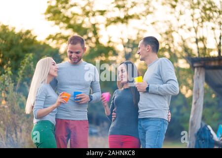Picnic con gli amici mediante il fuoco. Amici di società aventi una escursione picnic sullo sfondo della natura. Gli amici raccontano storie. Picnic estivo. Buon divertimento con gli amici. Foto Stock