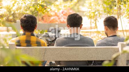 Vista posteriore di tre amici seduti sul tavolo occupato su mobile al parco - Concetto di migliori amici e stare insieme. Foto Stock