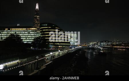 Vista dal Tower Bridge lungo il fiume Tamigi con il Municipio e la Shard sulla sinistra e il centro città di Londra a destra, illuminata di notte. Foto Stock