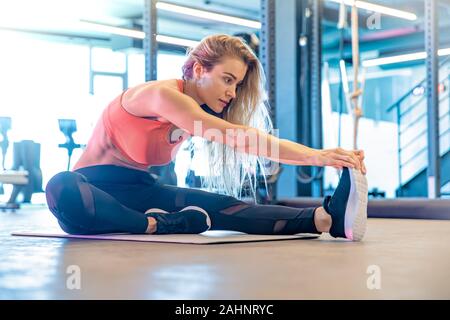 Giovane donna graziosa si allunga in palestra prima di esercizio Foto Stock