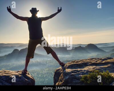 Summit achievemnt. Escursionista in nero celebrano il trionfo tra due picchi rocciosi. Splendida alba nelle montagne rocciose Foto Stock