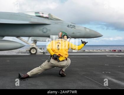 Stati Uniti Navy shooter Lt. Charles Kollar, dirige il lancio di un F/A-18E Super Hornet fighter aircraft attaccato al pugno della flotta di Strike Fighter Squadron 25 sul ponte di volo Nimitz-class portaerei USS Abraham Lincoln 28 dicembre 2019 operanti nel Mare delle Filippine. Foto Stock