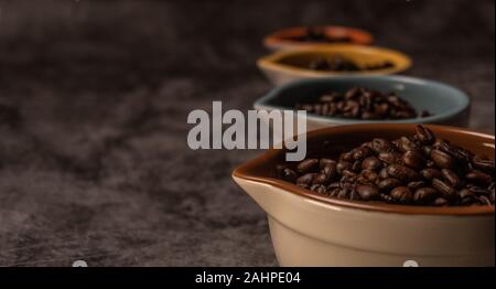 Vista laterale di freschi organici grezzi i chicchi di caffè all'interno di molte colorate tazze di ceramica Foto Stock