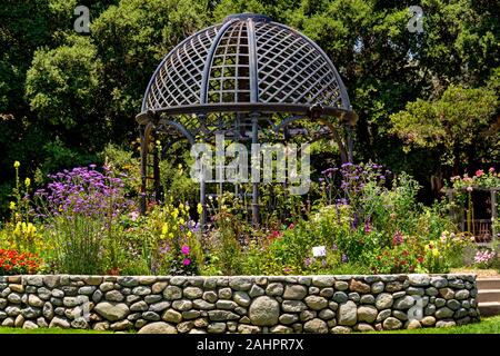 Grandi weathered ferro battuto gazebo è al centro di un giardino circondato da bellissimi fiori di primavera. Foto Stock