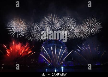 Fuochi d'artificio illuminano il cielo sopra il London Eye a Londra centrale durante i festeggiamenti di Capodanno. Foto Stock