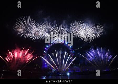 Fuochi d'artificio illuminano il cielo sopra il London Eye a Londra centrale durante i festeggiamenti di Capodanno. Foto Stock