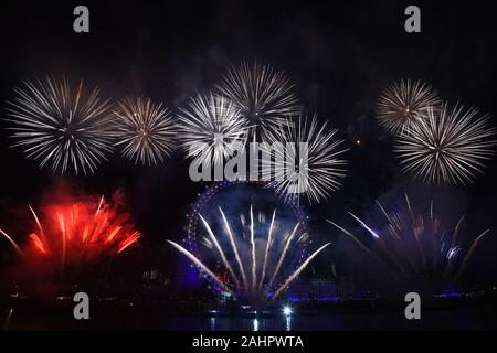 Fuochi d'artificio illuminano il cielo sopra il London Eye a Londra centrale durante i festeggiamenti di Capodanno. Foto Stock