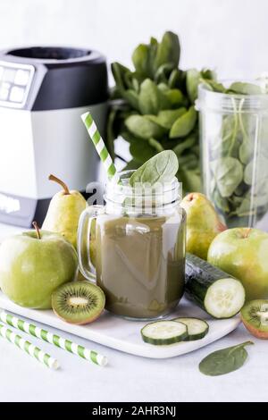 Una vista ravvicinata di un barattolo di vetro riempito con frullato di verde e circondato dal verde della frutta e della verdura utilizzate per fare il frullato. Foto Stock