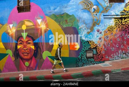 Uomo che cammina passato street art e graffiti dipinti su esterno dell edificio in Candelaria distretto di Bogotà, Colombia Foto Stock