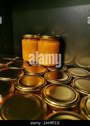 Allineamento del fustellato piccoli vasetti di vetro con oro tappi di metallo di marmellata fatta in casa su sfondo nero con riflessi di luce Foto Stock