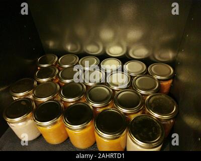 Allineamento del fustellato piccoli vasetti di vetro con oro tappi di metallo di marmellata fatta in casa su sfondo nero con riflessi di luce Foto Stock