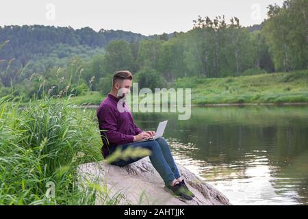 Lavoro uomo che lavora sul computer portatile durante le vacanze, il lavoro remoto, vista dal retro. Libero professionista. Foto Stock