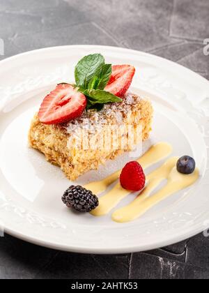 Napoleone tradizionale pasta torta con crema alla vaniglia e frutti di bosco, guarnito con fragole e menta in un ristorante che serve. Cucina russa, layere Foto Stock