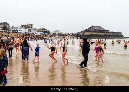 Il Capodanno annuale nuota in mare a Broadstairs sulla costa del Kent in Inghilterra. Gli spettatori delle folle si sono riuniti sul litorale della spiaggia, guardando come alcuni dei nuotatori ritornano dopo il loro tuffo freddo in mare. Broadstairs porto sullo sfondo. Foto Stock