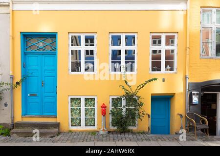 Copenhagen, Danimarca: caratteristico e colorato giallo / arancio dipinto casa di città con porte blu e bianco finestre incorniciate da una pavimentazione in ciottoli. Foto Stock