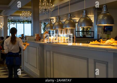 Le luci di una piastra calda o cibo passano in un ristorante con una cameriera che trasportano le piastre è passato Foto Stock