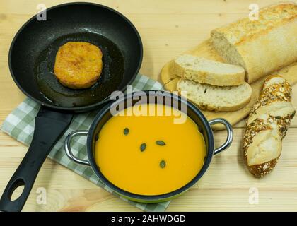 Zuppa di zucca in una pentola, patty in una padella con la ciabatta e i semi di zucca rotoli Foto Stock