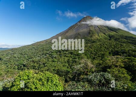 Il Vulcano Arenal in Costa Rica in una giornata di sole con cielo blu e la foresta pluviale in primo piano.Arenal Volcano National Park, provincia di Alajuela, Costa Rica Foto Stock