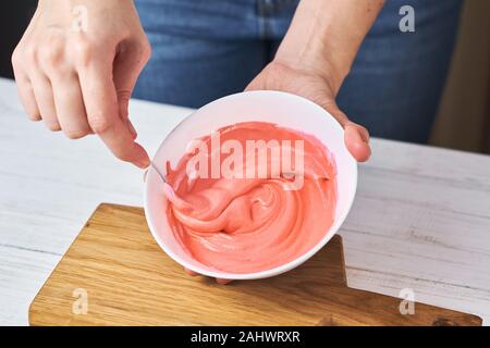 Donna colore rosso sbattere la panna per decorare i cookie in un recipiente da cucina, primo piano Foto Stock