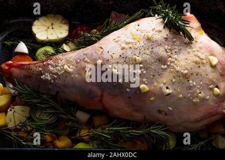 La gamba di agnello pronti per la tostatura con sale, aglio, rosmarino, verdure e aglio, paesaggio, vicino. Foto Stock