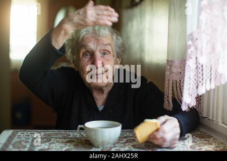 Anziani vecchia donna bere il tè con biscotti a casa. Foto Stock
