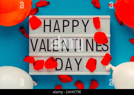 Happy Valentines Day lightbox messaggio rosso con petali di fiori e palloncini. L'immagine orizzontale. Vista dall'alto. Foto Stock