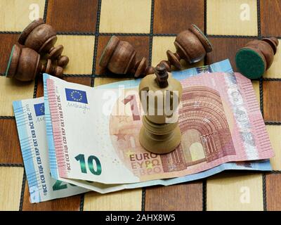 Regole di denaro concetto: Re Pezzo degli scacchi in piedi sulle banconote in euro con sconfitto giacenti pedine di una scacchiera Foto Stock