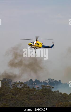 Bell 412 elicottero volando contro pennacchi di fumo durante la lotta contro gli incendi di bush in Victoria, Australia. Foto Stock