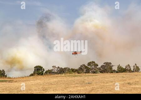 Erickson Air Crane elicottero N243AC (Sikorsky S-64) volare contro pennacchi di fumo durante la lotta contro gli incendi di bush in Victoria, Australia. Foto Stock