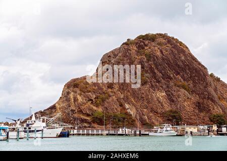 Una marina costiera con barche ormeggiate di fronte ad una grande roccia del vulcano di lava plug Foto Stock