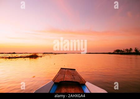 Thai barca dalla coda lunga centina anteriore in pacifica di Nong Harn lago, Udonthani - Thailandia. La barca di legno sotto la vibrante bellissima alba cielo sopra red lotus lake. Foto Stock