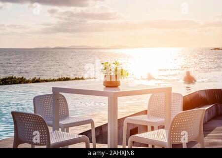 Tavolo con sedie accanto a un infinity edge laguna bagnata in morbido di prima mattina dalla luce attraverso l'oceano, una tranquilla vista in Australia. Swimm Foto Stock