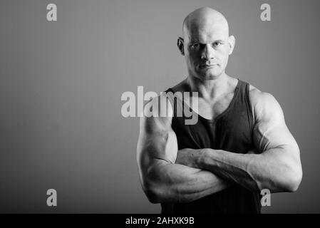 Bald muscolare di uomo che indossa serbatoio superiore contro lo sfondo grigio Foto Stock