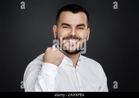 Giovani felici bello uomo barbuto pugno di sollevamento su sfondo nero. eccitato esprimenti il gesto vincente Foto Stock