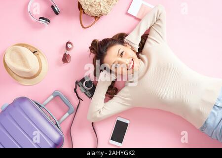 Donna di viaggio sorriso felicemente e cercare da qualche parte giacente sul piano di colore rosa. Vista superiore Foto Stock